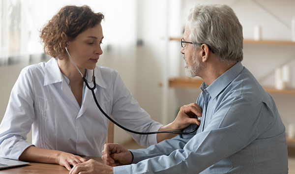 Doctor with stethoscope checking adult man's heart